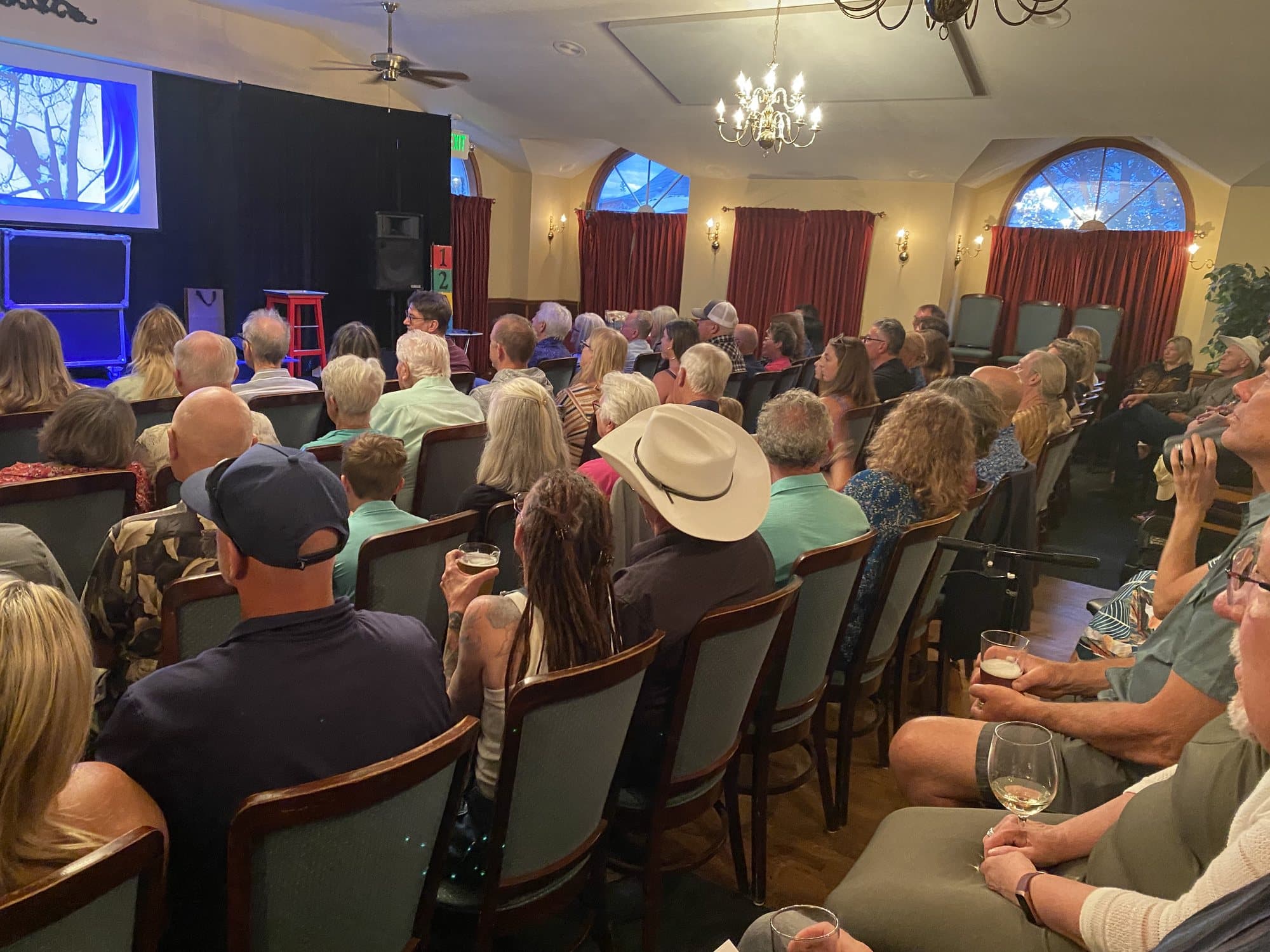 A full house inside the Magic Manor showroom, chandeliers overhead, watching the stage